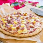 freshly baked hawaiian pizza with pineapple, ham, and bacon on a cutting board