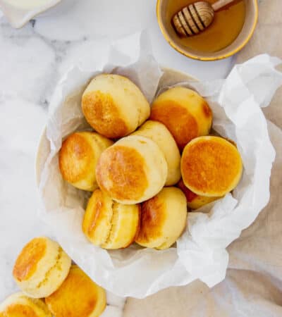 Homemade Biscuits Piled Into a Bowl Next to More Biscuits and a Small Bowl of Honey