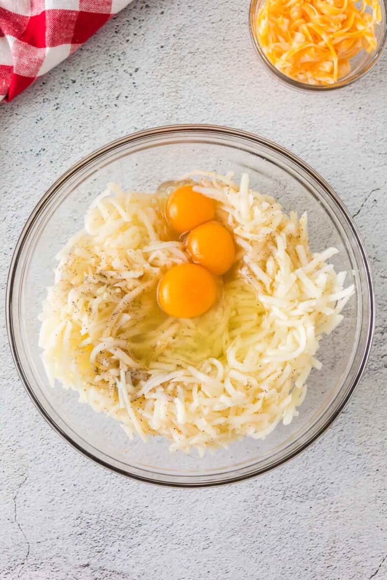 shredded potatoes, eggs, and seasonings unmixed in a glass mixing bowl