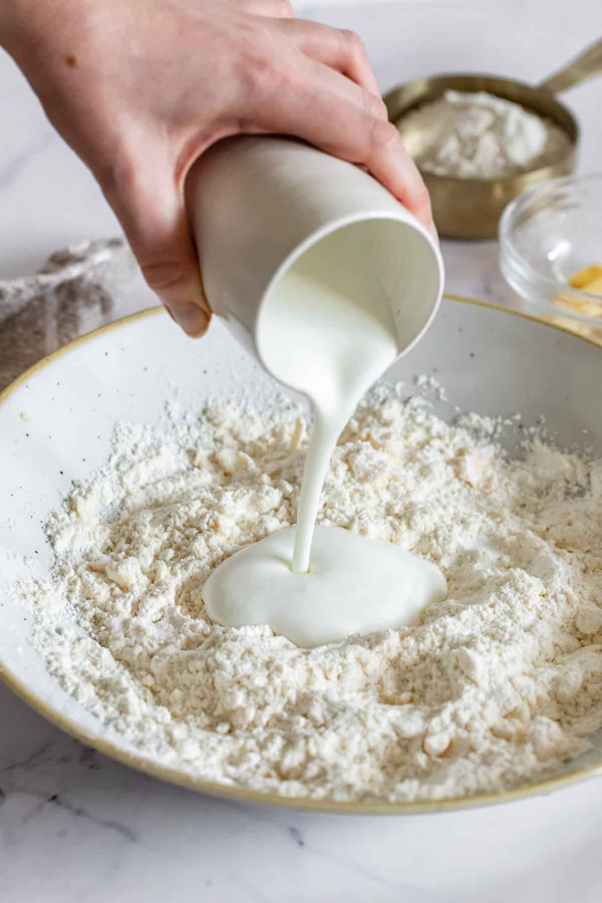 Buttermilk Being Poured into a Tan-Rimmed Bowl Filled with the Flour Mixture