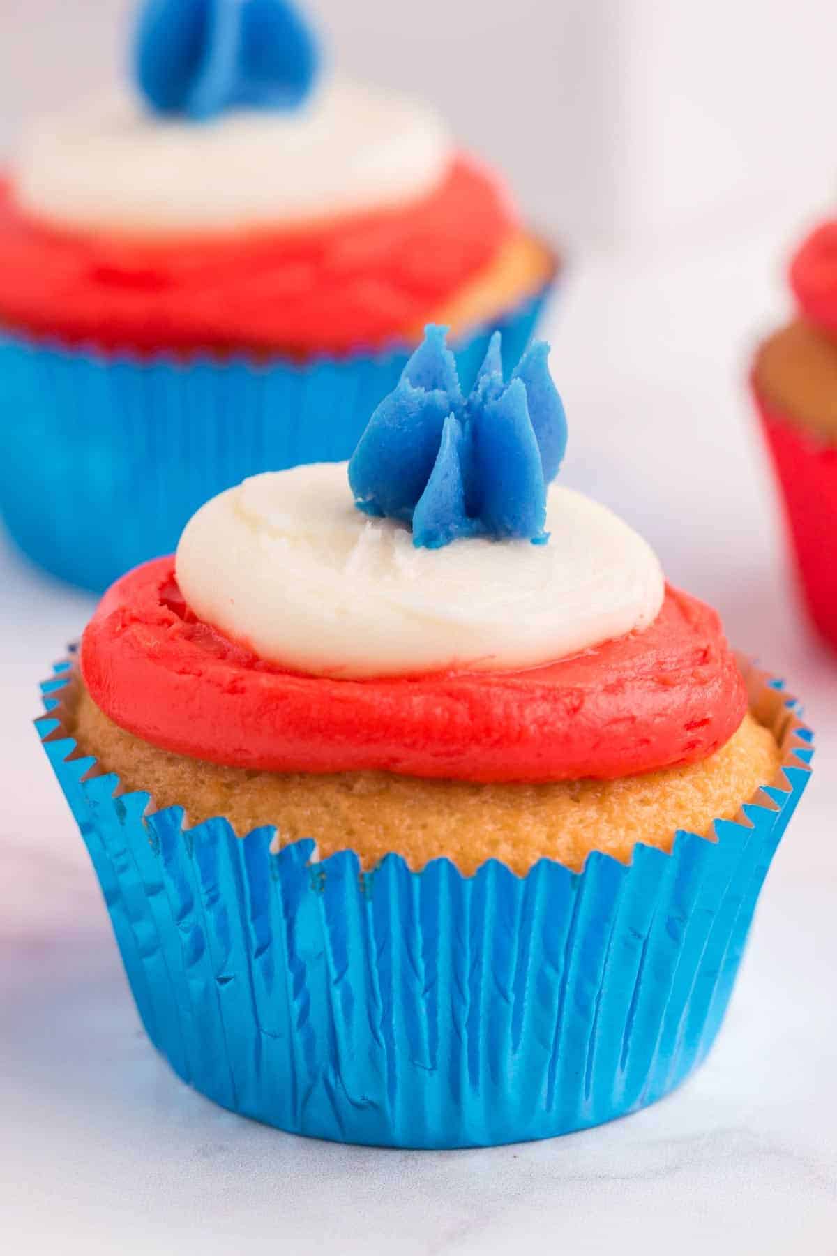 one fourth of july cupcake with a layer of red, a layer of white and a piped star of blue frosting in a blue foil liner