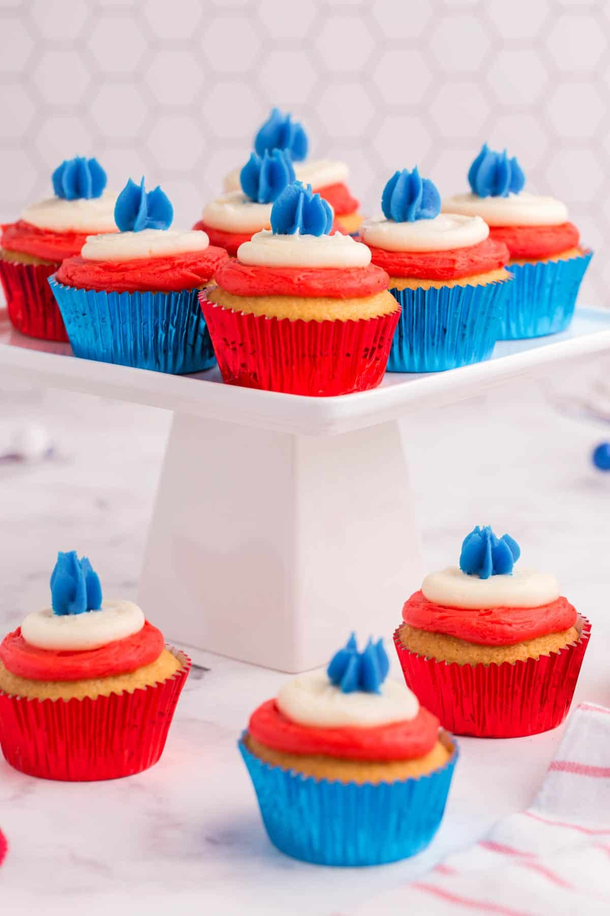 4th of july cupcakes in red and blue foil liners on top of and next to a white cake stand
