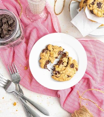 Two Halves of a Gluten Free Chocolate Chip Cookie on a Plate Beside Three Metal Forks