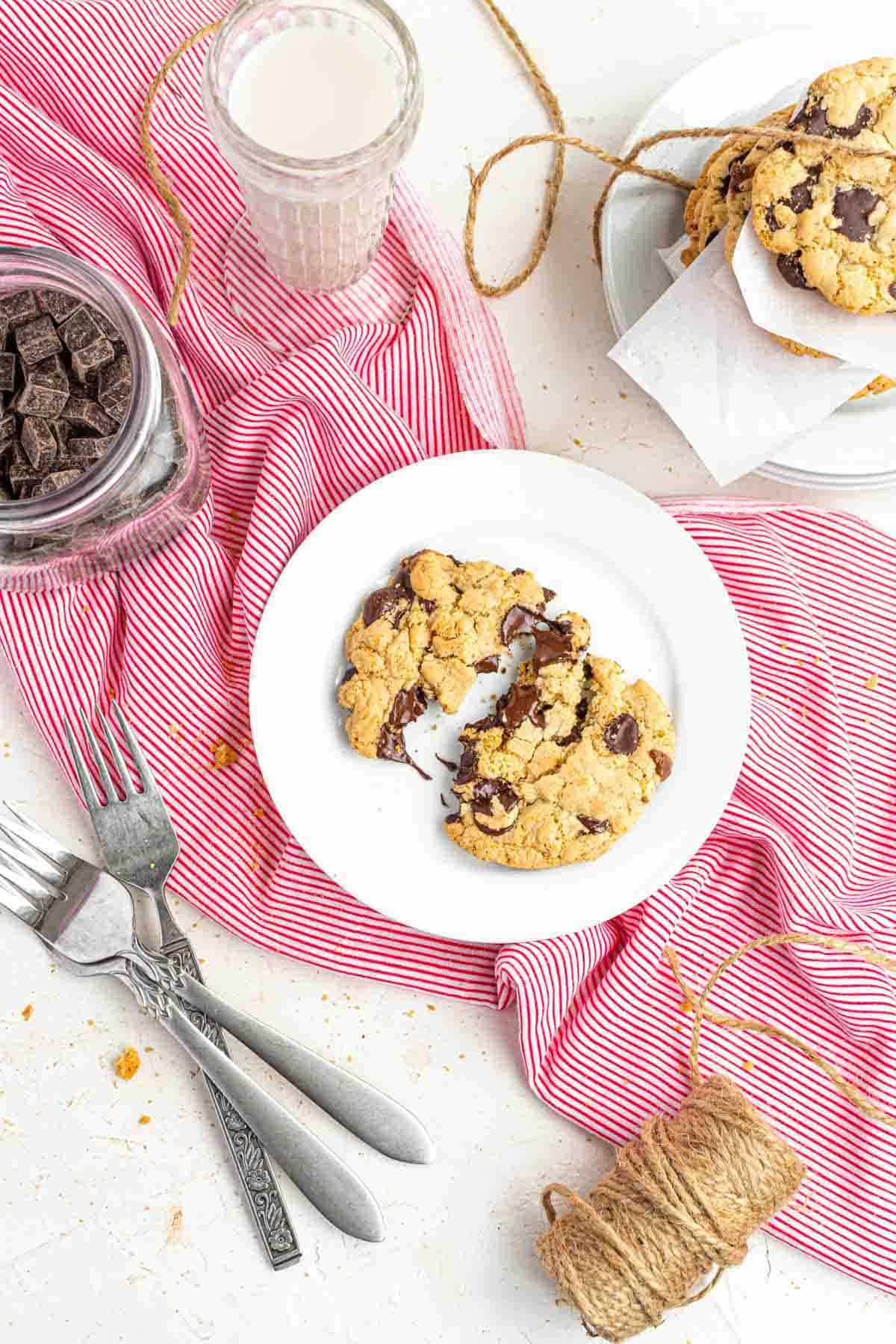 Two Halves of a Gluten Free Chocolate Chip Cookie on a Plate Beside Three Metal Forks