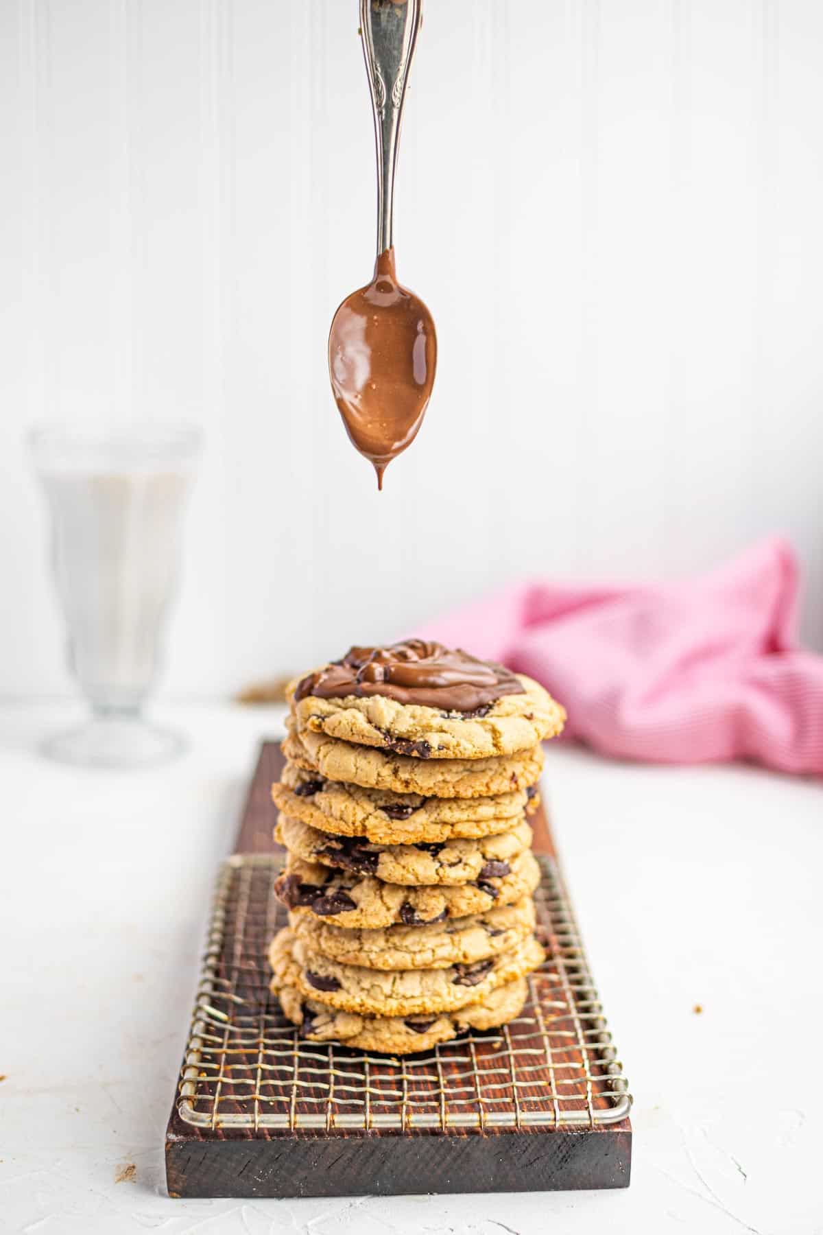 A Spoon Holding Melted Chocolate Above a Stack of Homemade Chocolate Chip Cookies