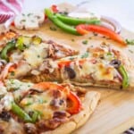 sliced supreme pizza on a cutting board with one slice being pulled away