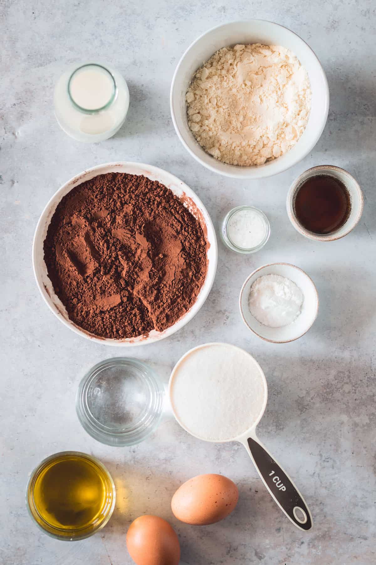 A Bowl of Cocoa Powder, A Bowl of Gluten-Free Flour, a Cup of Granilated Sugar, Two Eggs and the Rest of the Cupcake Ingredients on a Countertop