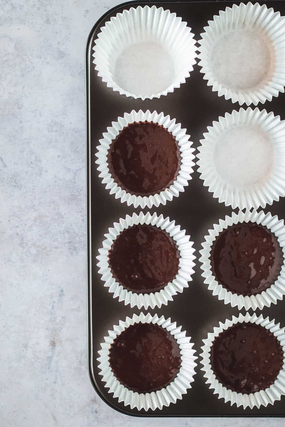 Eight Cupcake Liners in a Pan, Five of Which are Filled Two Thirds of the Way Full with Batter