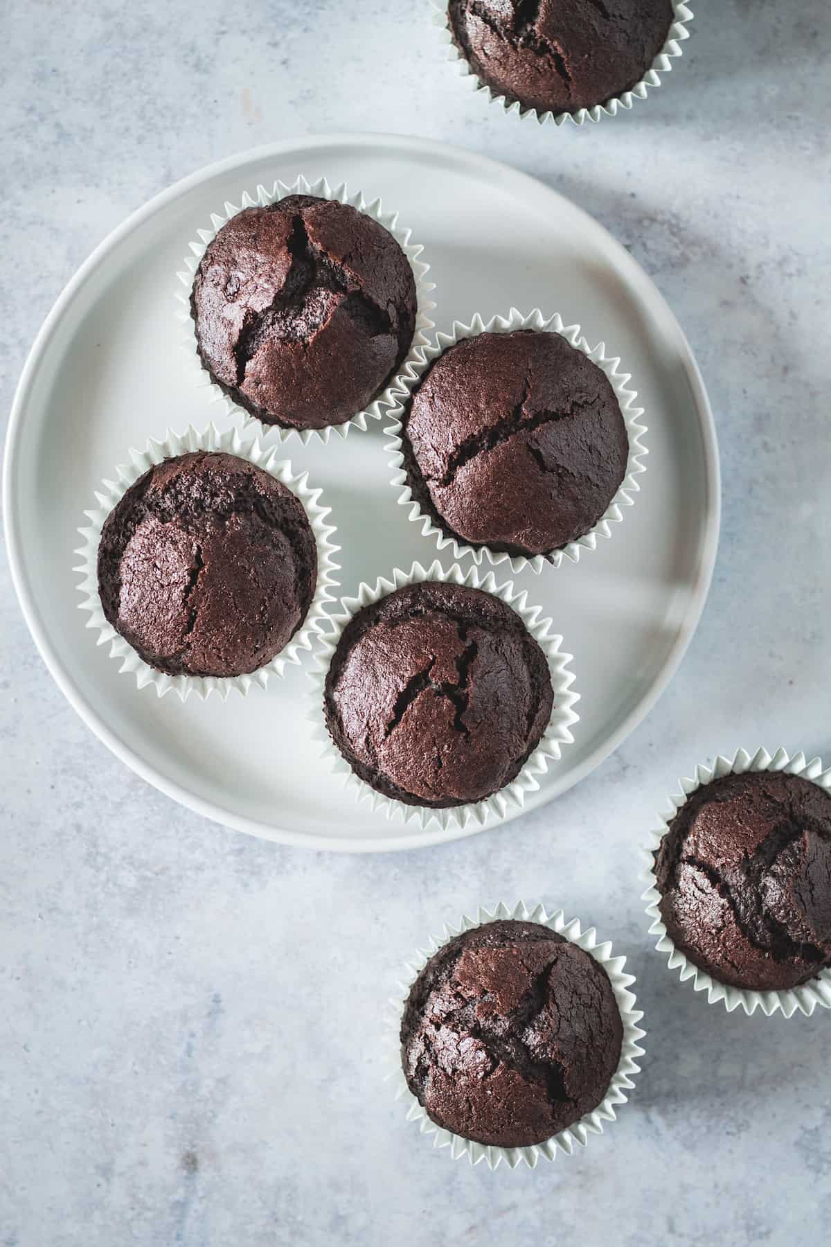 A Bird's Eye View of a Plate of Unfrosted Chocolate Cupcakes with Three Stray Cupcakes Next to the Plate