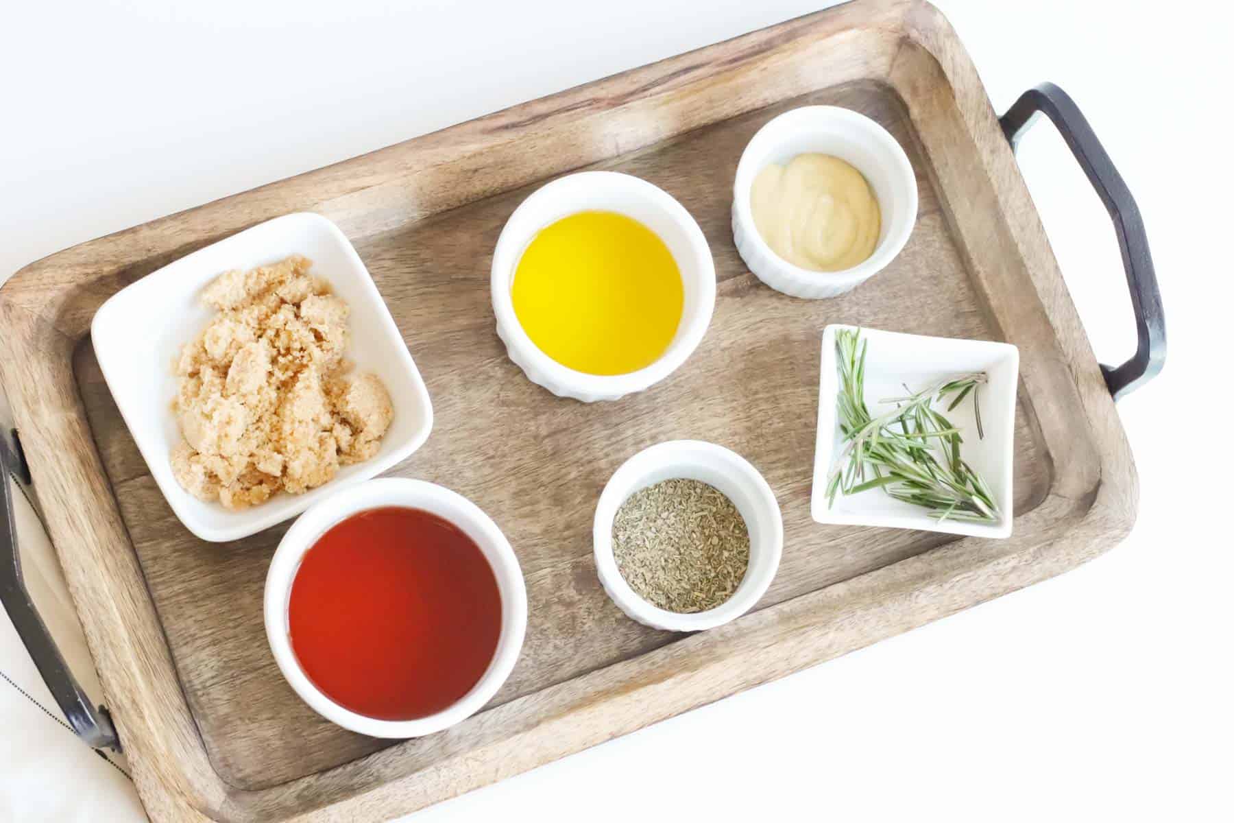 bowls of red wine vinegar, olive oil, dijon mustard, dried Italian seasoning, brown sugar, and fresh rosemary on a wooden serving tray