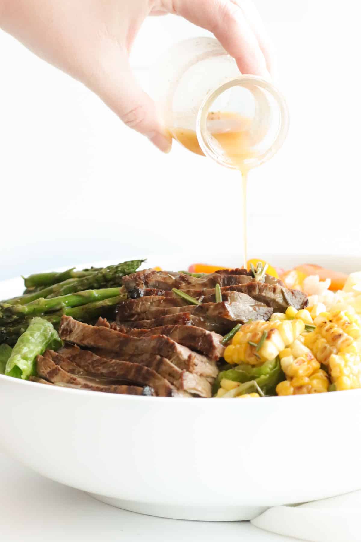 pouring the dressing over a big bowl of steak salad