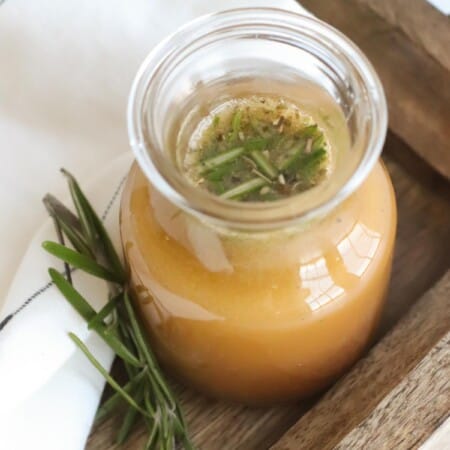 bottle of red wine vinegar dressing on a wooden tray next to a sprig of rosemary