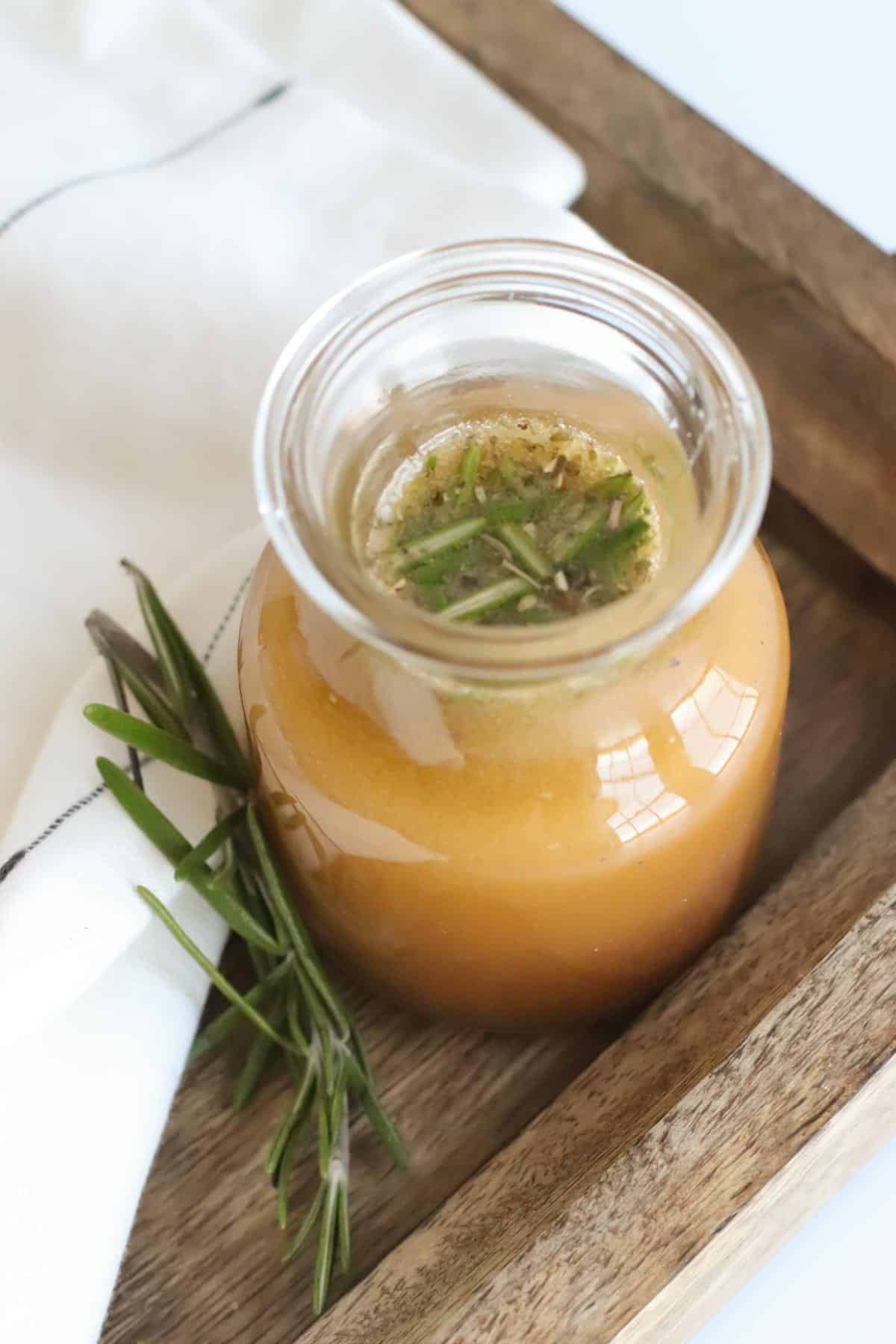 bottle of red wine vinegar dressing on a wooden tray next to a sprig of rosemary