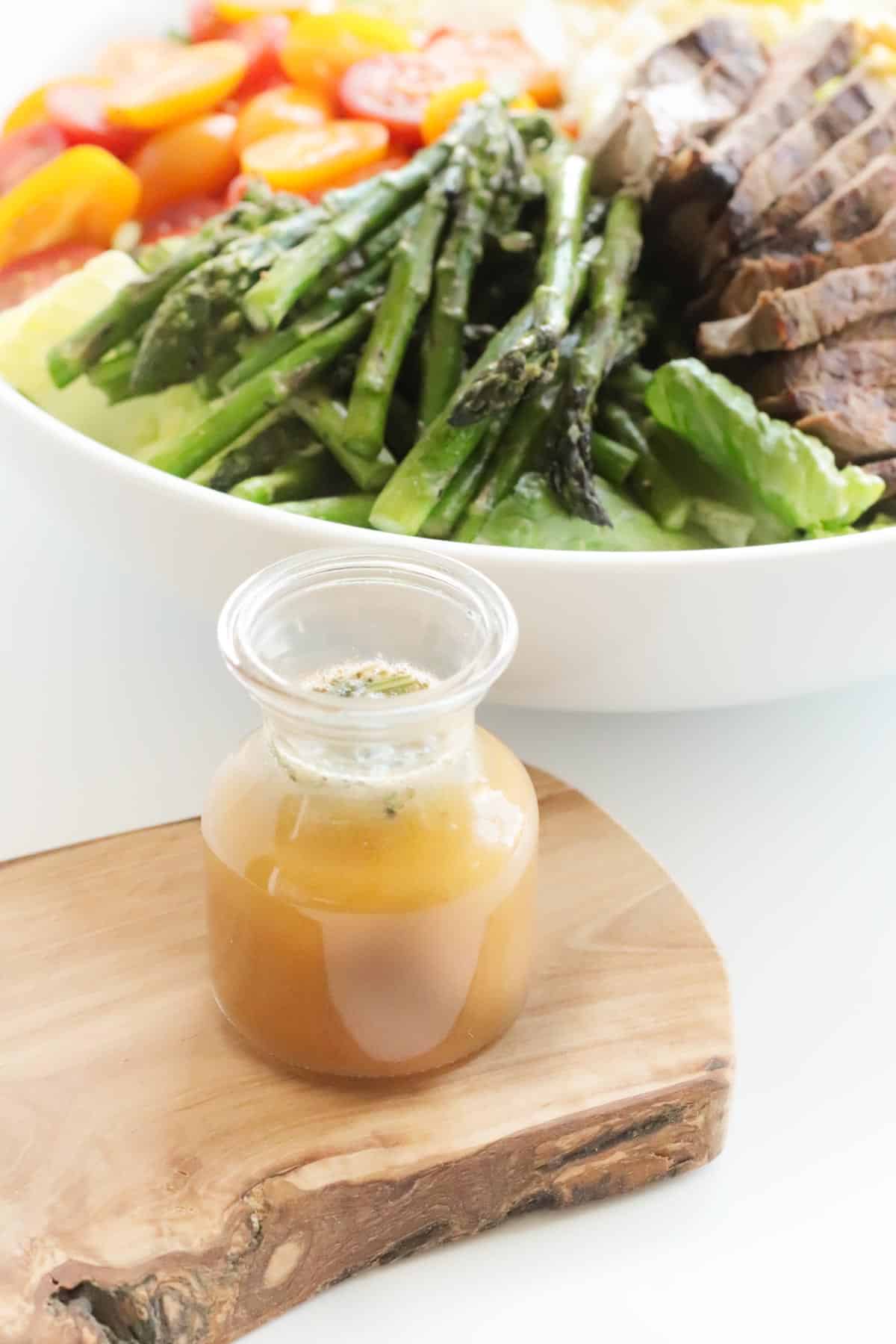 red wine vinaigrette on a natural wood serving board next to a bowl of salad