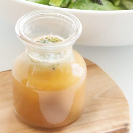 bottle of red wine vinaigrette dressing on a wooden board next to a bowl