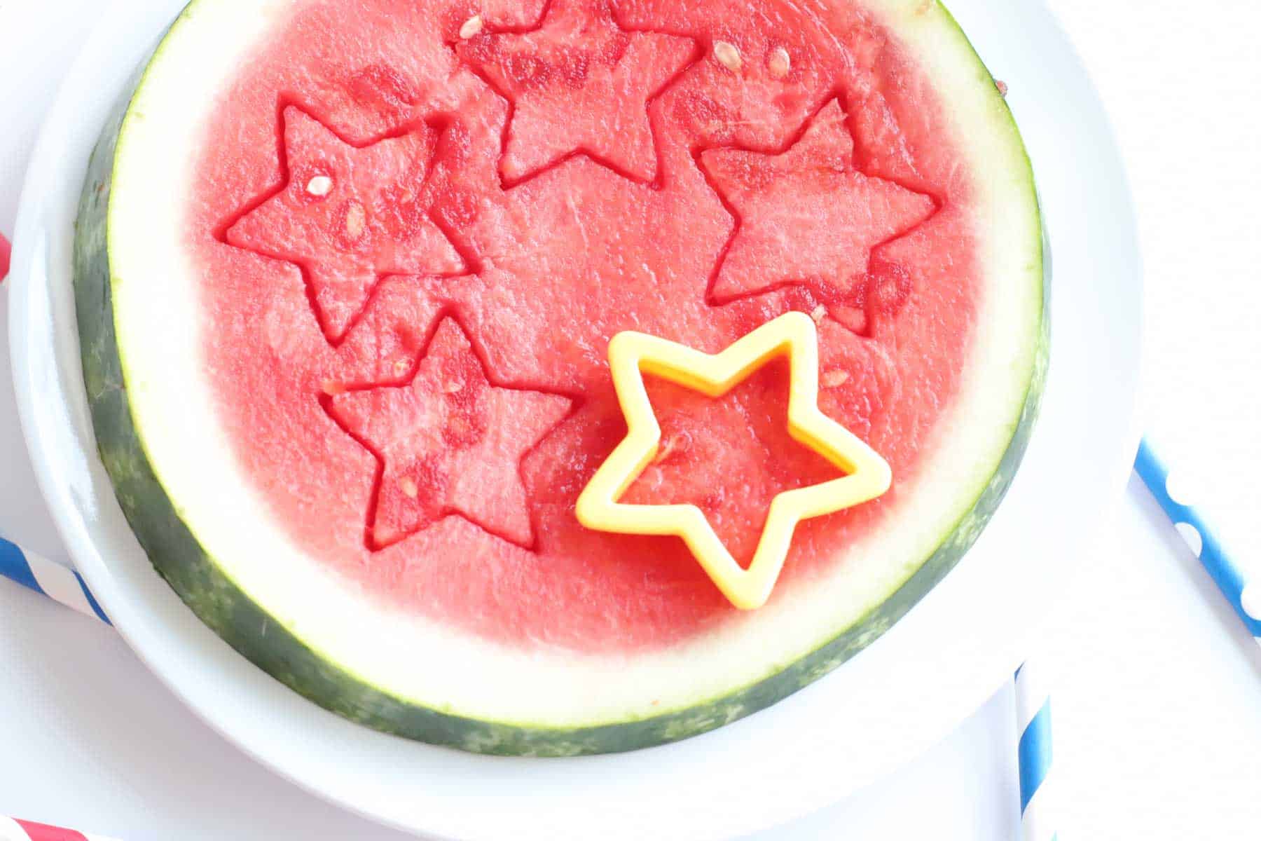 yellow star-shaped cookie cutter cutting stars out of a round slice of watermelon