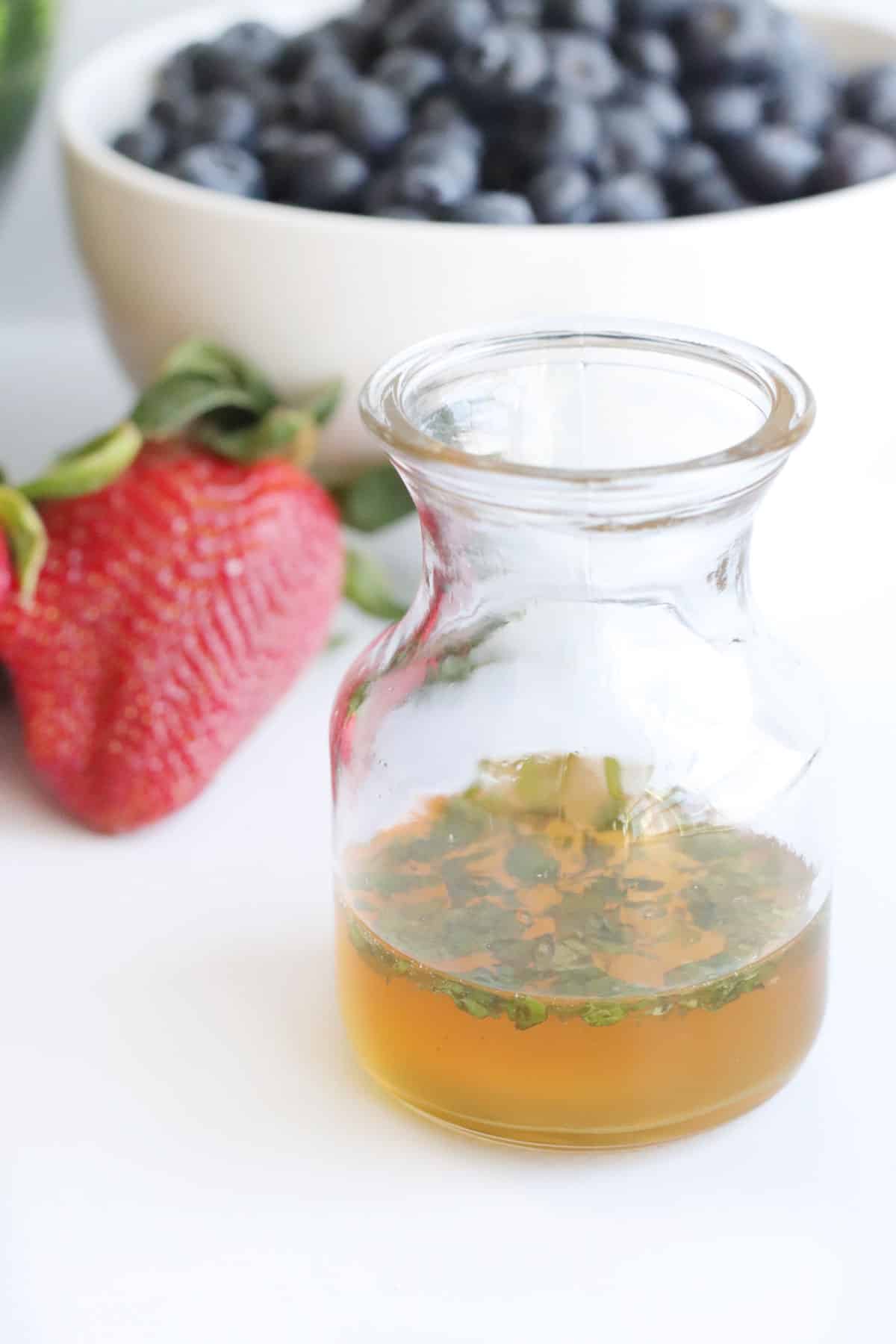 small glass bottle of honey lime dressing with mint leaves