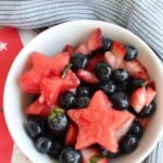 small bowl of fruit salad with chopped strawberries, blueberries, and watermelon stars surrounded by red ad white star napkins and a blue stripe cloth napkin