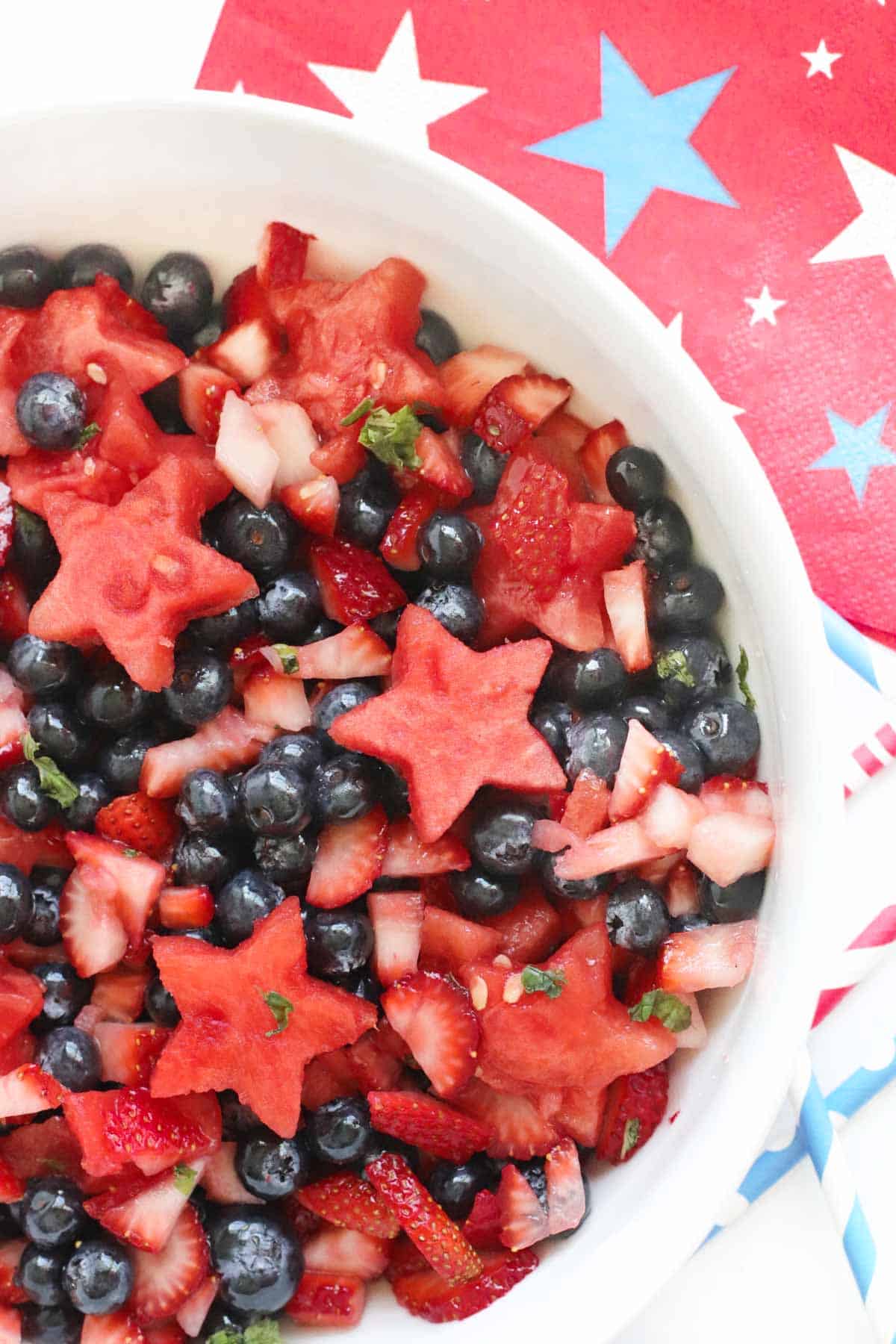 watermelon berry fruit salad in a white bowl surrounded by patriotic napkins and straws