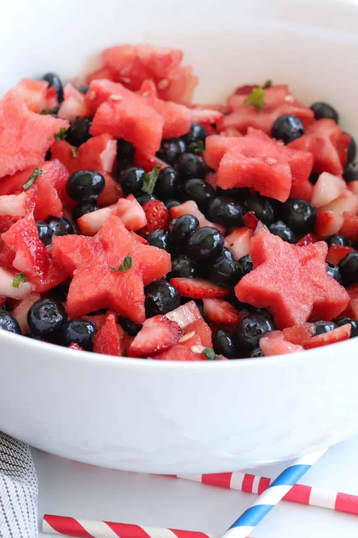 white bowl filled with a red, white, and blue berry fruit salad with strawberries, blueberries, and watermelon cut into star shapes