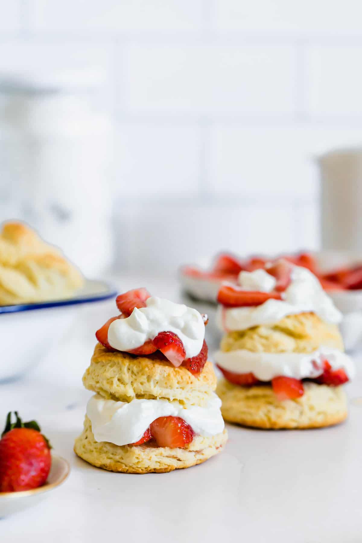 Two Side-by-Side Gluten Free Strawberry Shortcakes in Front of a Bowl of Sweet Biscuits