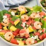 A bowl of salad topped with shrimp, fruit, goat cheese, pine nuts, and strawberry poppyseed dressing with text overlay that says "Summer Fruit Grilled Shrimp Salad".