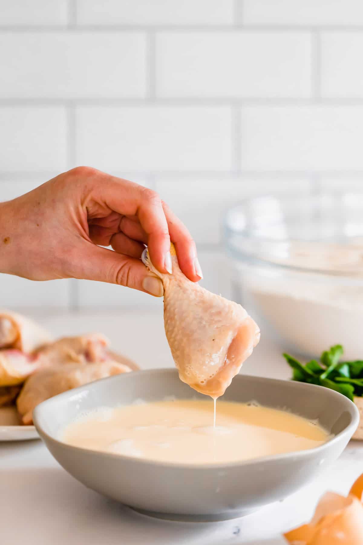 A Raw Chicken Leg Being Dipped Into the Bowl of Whisked Milk and Eggs