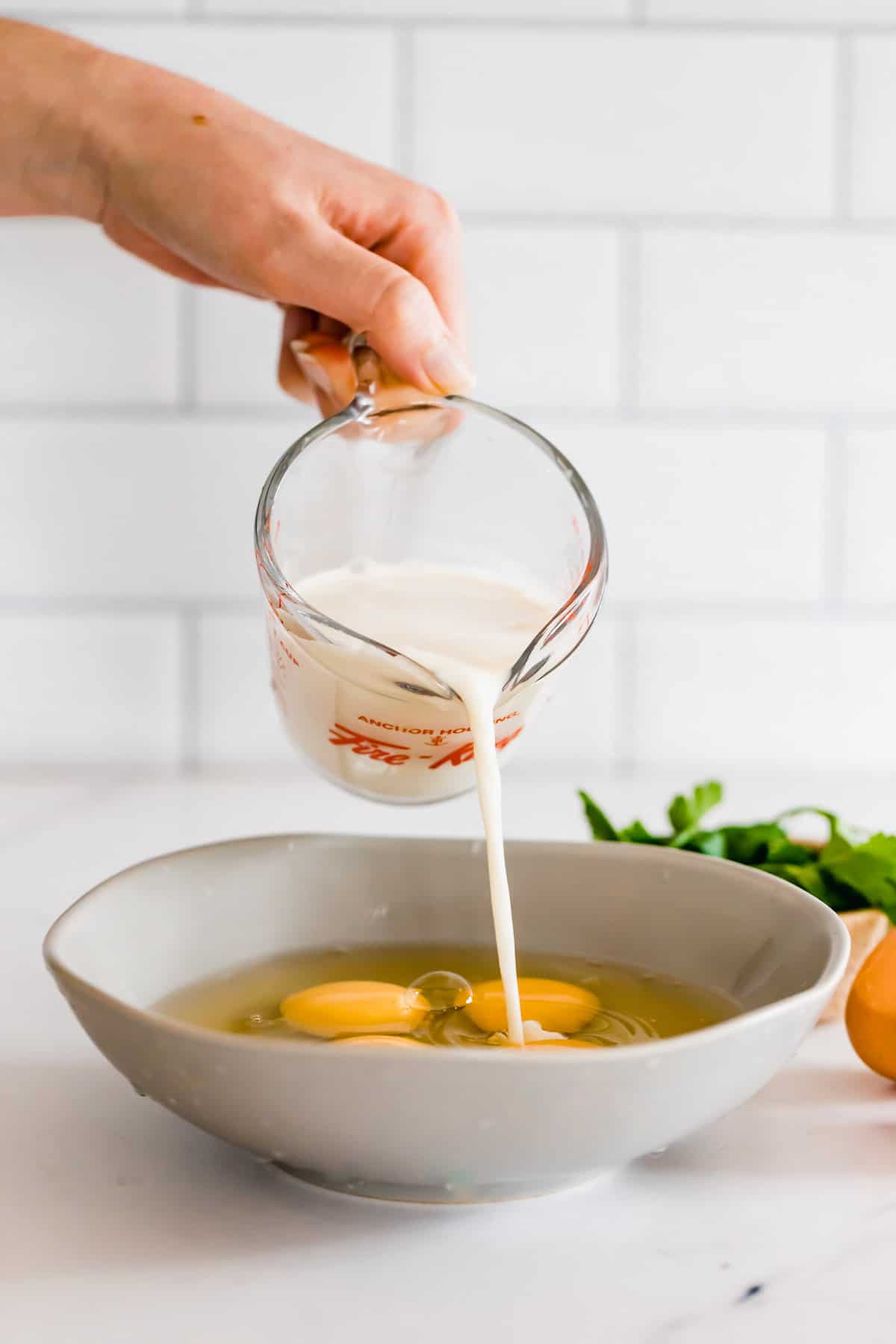 A Hand Pouring Milk From a Measuring Cup Into a Bowl of Eggs