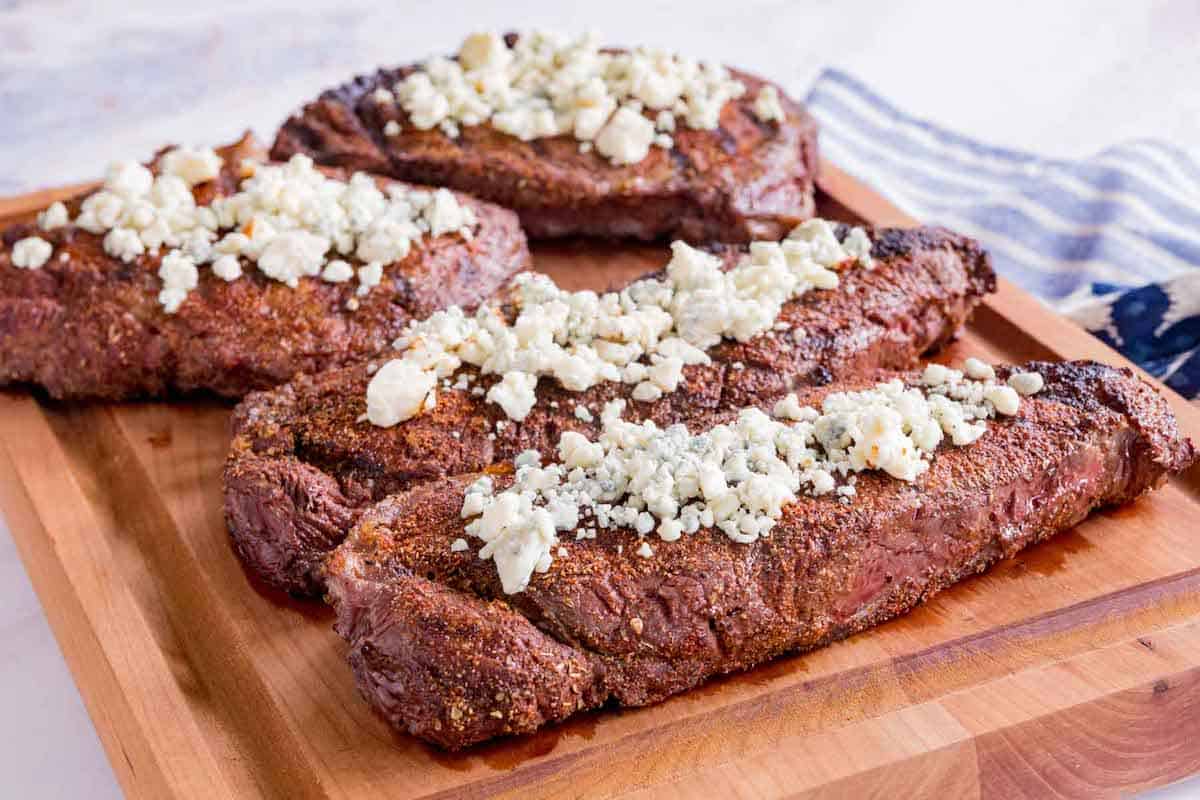 blackened steaks with blue cheese on top on a cutting board
