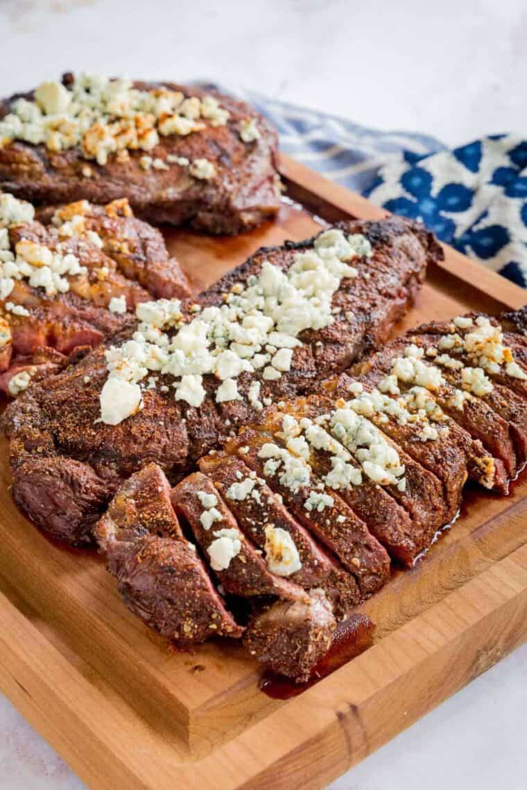 Slices of Black and Blue Steak on a Wooden Cutting Board Beside Whole Pieces of Steak