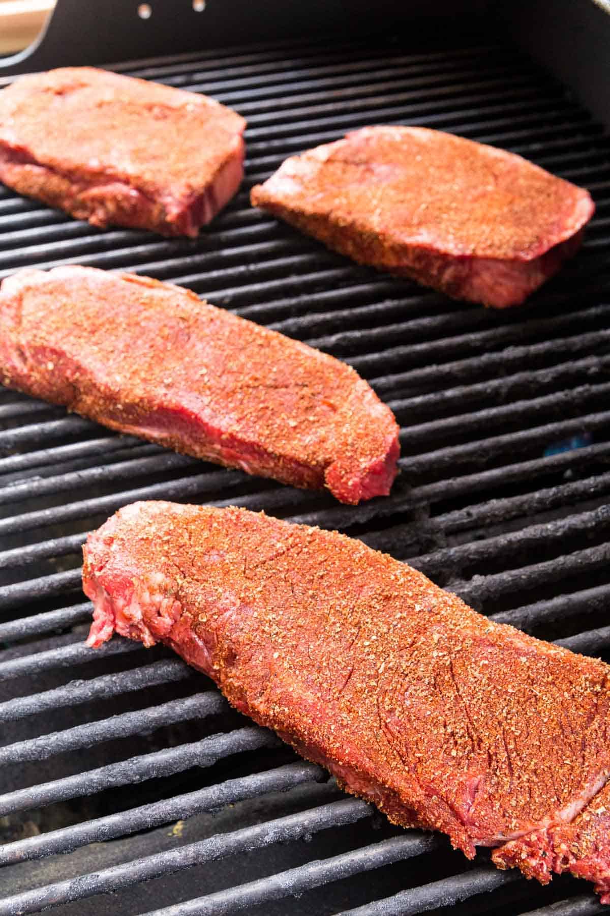 Four Spice-Rubbed Steaks Cooking on a Grill