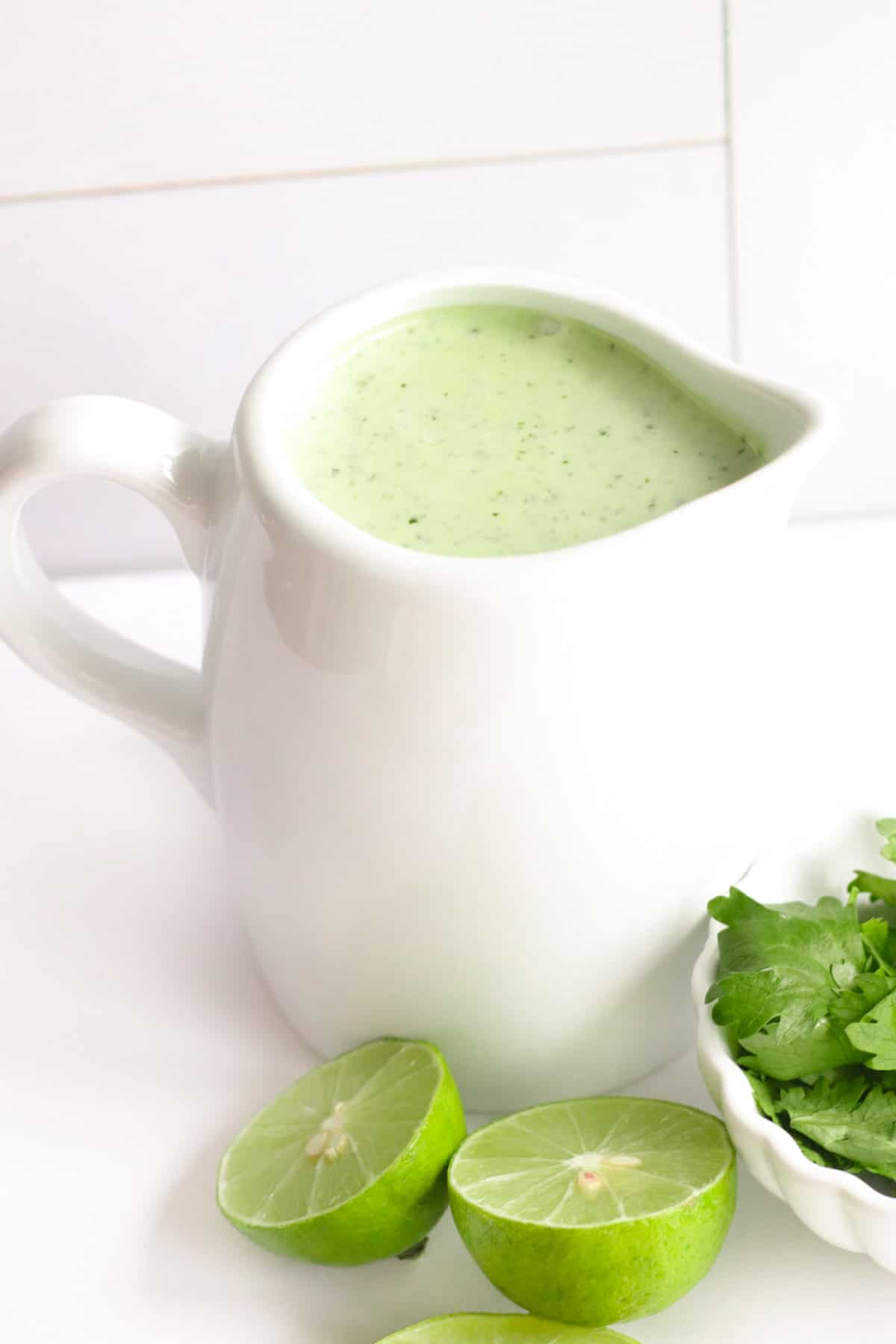 jalapeno ranch dressing in a white container for pouring nest to a dish of cilantro and limes