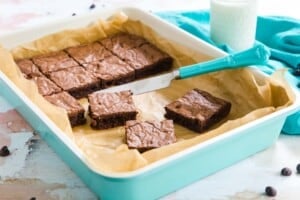 turquose baking pan lined with parchment with some of the cut brownies and a small knife in it