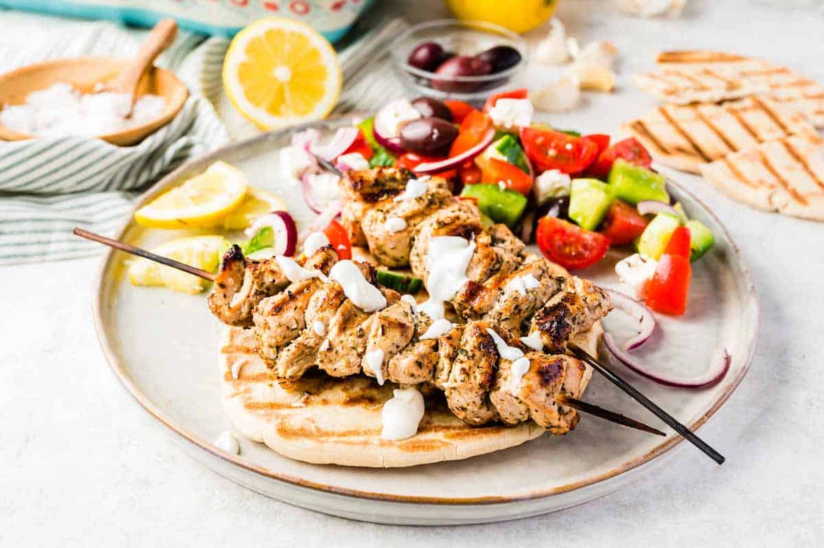 Grilled chicken skewers on pita on a plate with Greek salad