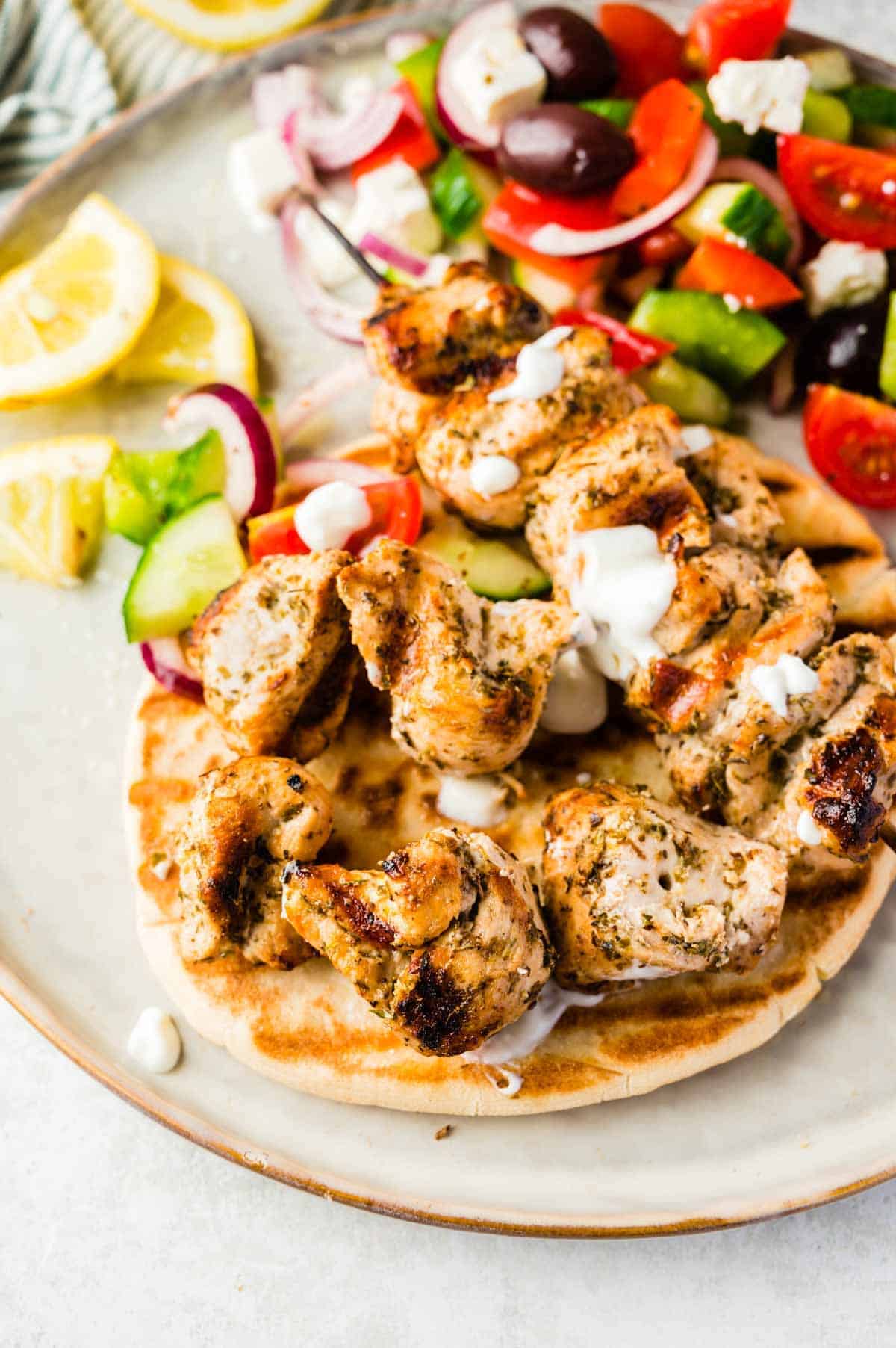 Chicken Souvlaki on Top of Grilled Pita Bread on a Plate with Greek Salad