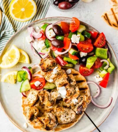 Chicken kabobs on a plate alongside greek salad.
