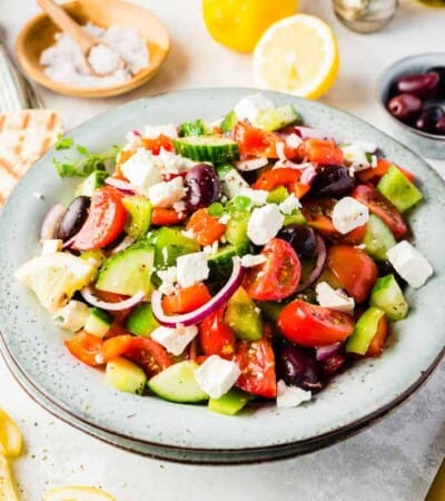 Two Doubled-Up Bowls Containing Greek Salad with Pita Bread and Spoons Beside Them