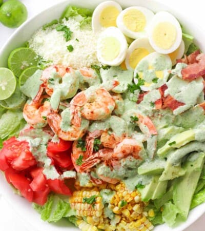 Shrimp Cobb Salad with hard boiled eggs, bacon, limes, tomatoes, avocado, cotija cheese, grilled corn, and cilantro lime dressing in a white serving bowl