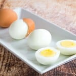 a rectangular white plate with one hard boiled egg in the shell, one with the shell cracked and partially removed, one peeled, and one peeled and cut in half