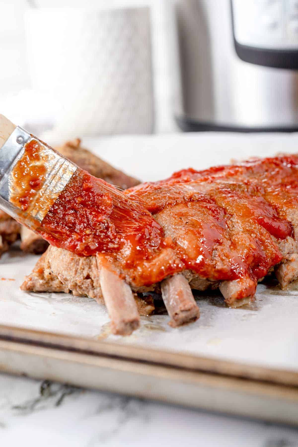 A Pastry Brush Adding Apple Honey BBQ Sauce to a Set of Baby Back Ribs on a Pan