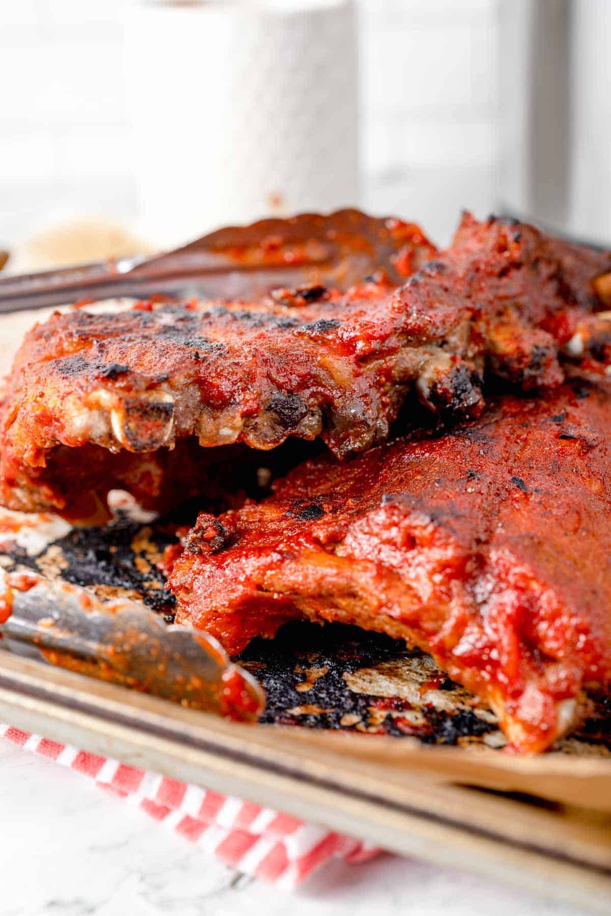 Two racks of barbecue ribs stacks in a parchment-lined sheet pan.