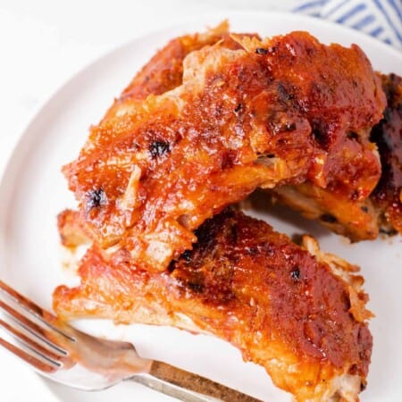 A White Plate Holding Baby Back BBQ Ribs and a Metal Fork