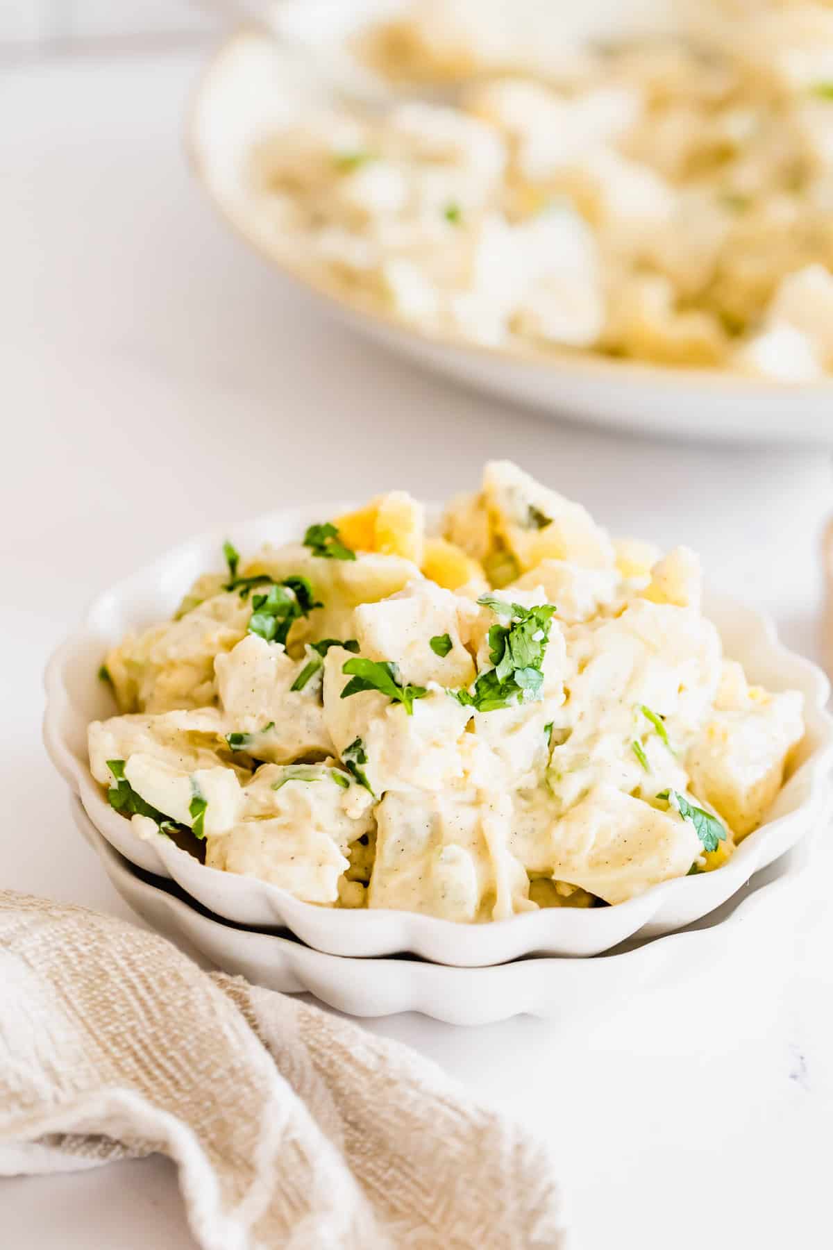 A Serving of Instant Pot Potato Salad in a Bowl with a Larger Plate of Potato Salad Behind it
