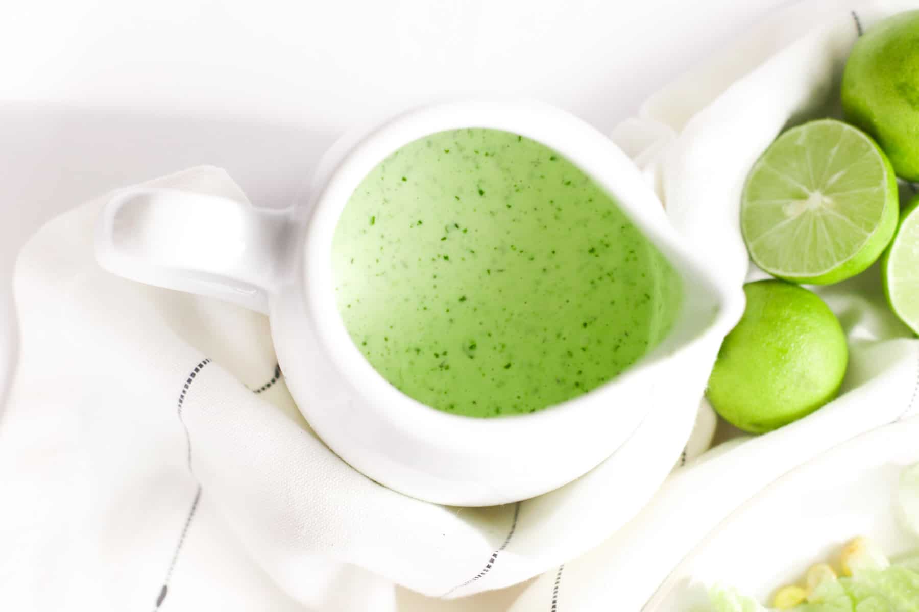 looking down into a pitcher of jalapeno ranch dressing with limes in a napkin next to it