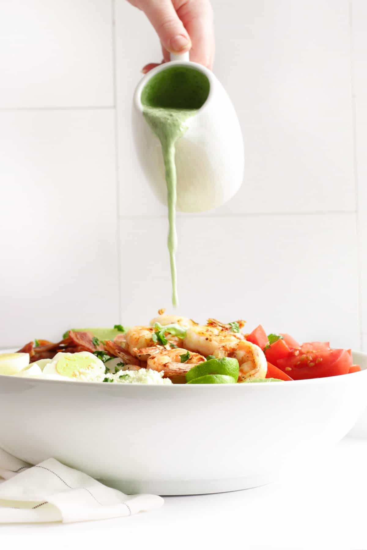 pouring jalapeno ranch dressing over a salad topped with shrimp, tomatoes, eggs, and bacon