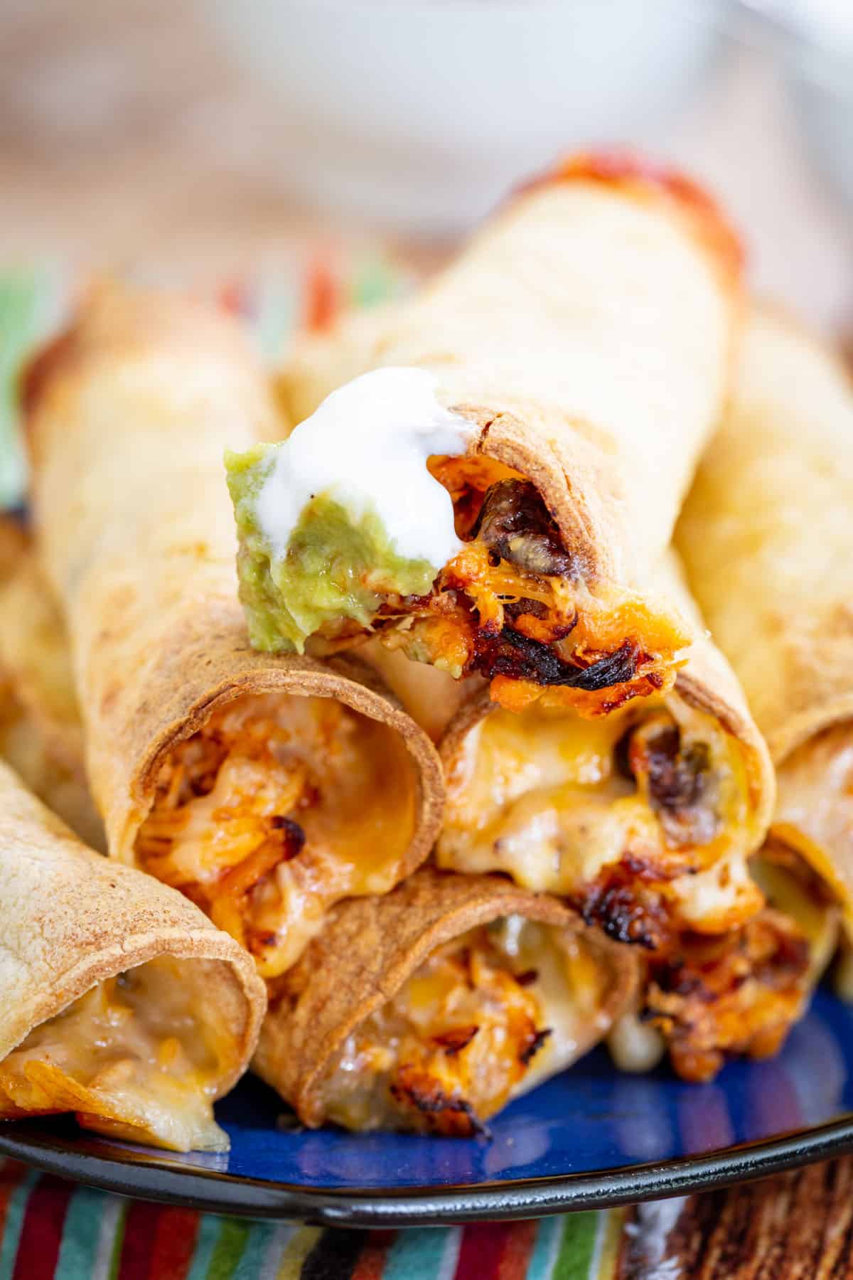 chicken and black bean taquitos on a blue plate with the top one dipped in guacamole and sour cream