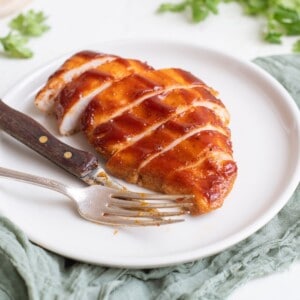 sliced bbq chicken on a white plate with a fork and knife