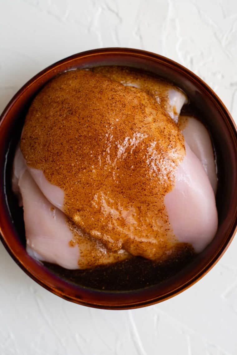 seasoned oil poured on top of the uncooked chicken in a bowl