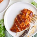 sliced chicken breast covered in barbecue sauce on a white plate with a fork and knife