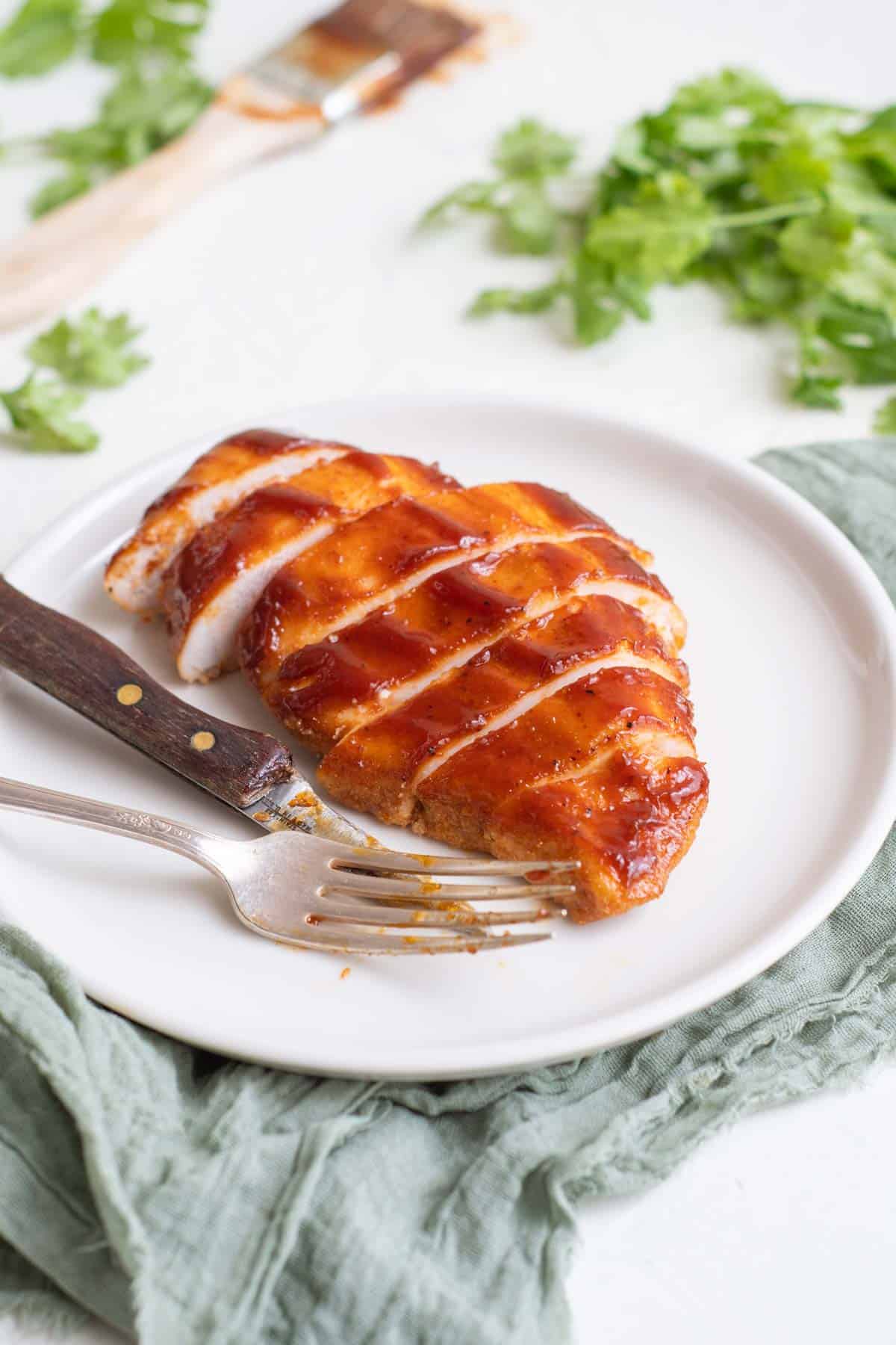 bbq chicken breast on a white plate with a fork and a knife